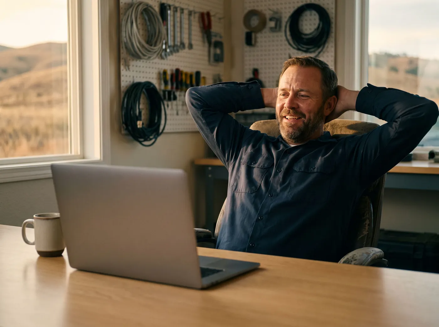 An electrical contractor leaning back in his chair with a relieved grin, hands behind his head